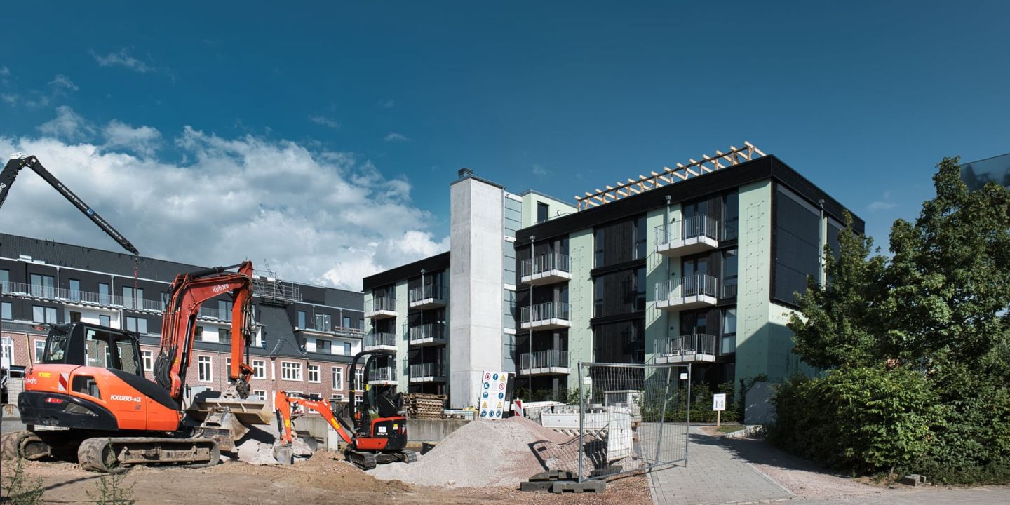 Baustelle im Wohnungsbau mit Bagger vor einem neu errichteten Mehrfamilienhaus